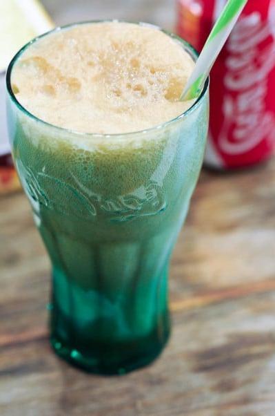 Κλασικό Κόκα-Κόλα με Παγωτό 5 Coke float σε πράσινο ποτήρι Coca-Cola με καλαμάκι και κόκκινο-άσπρο κουτί Coca-Cola στο παρασκήνιο.