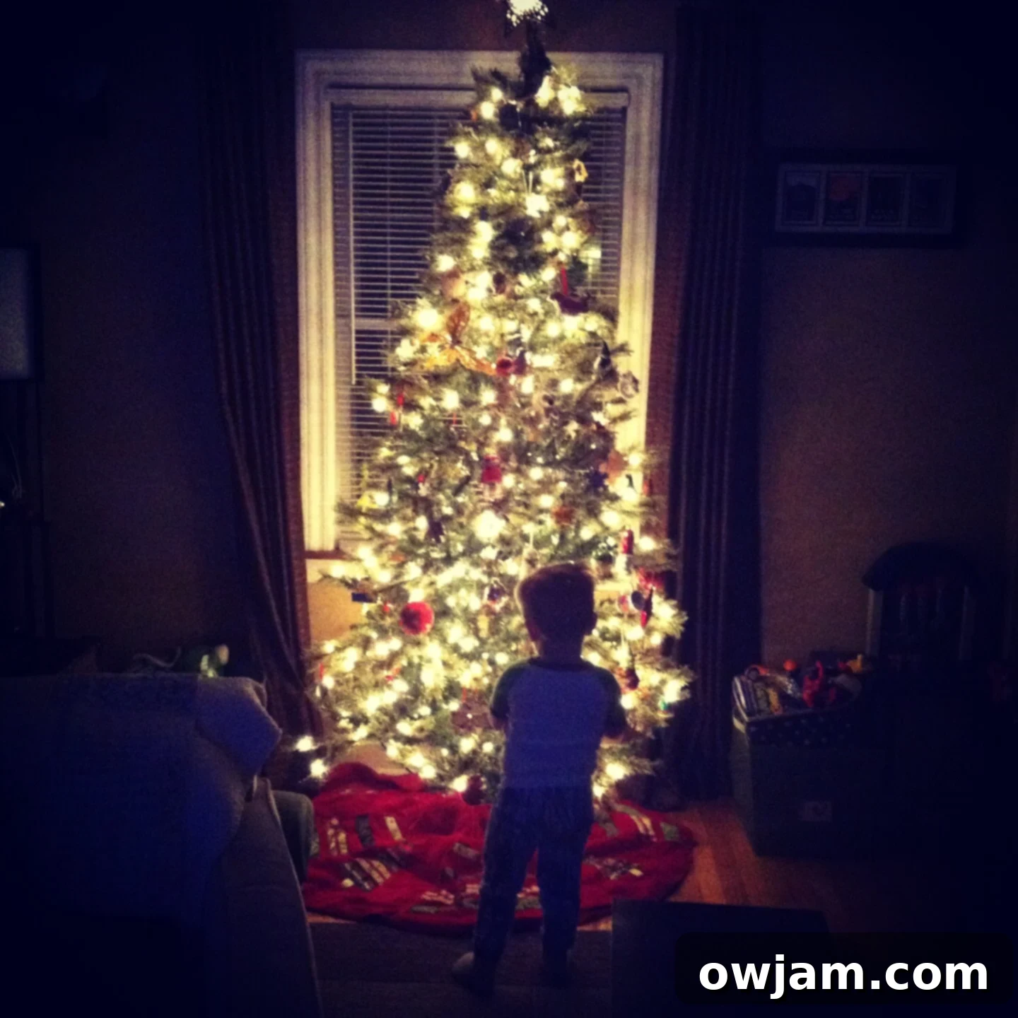 A toddler gazing in awe at a brightly lit Christmas tree adorned with festive ornaments.
