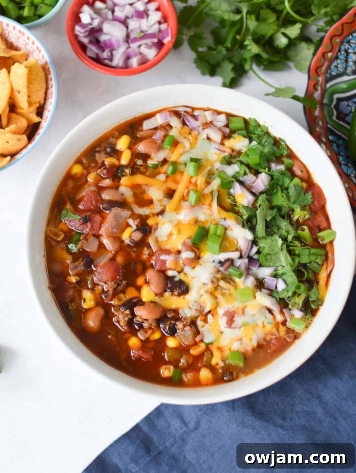 Slow Cooker Taco Soup Recipe in a white bowl with a blue napkin, topped with sour cream and cilantro