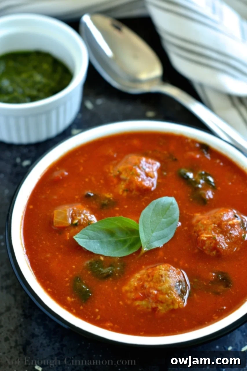 Hearty Spinach and Tomato Soup with Meatballs and fresh basil garnish.