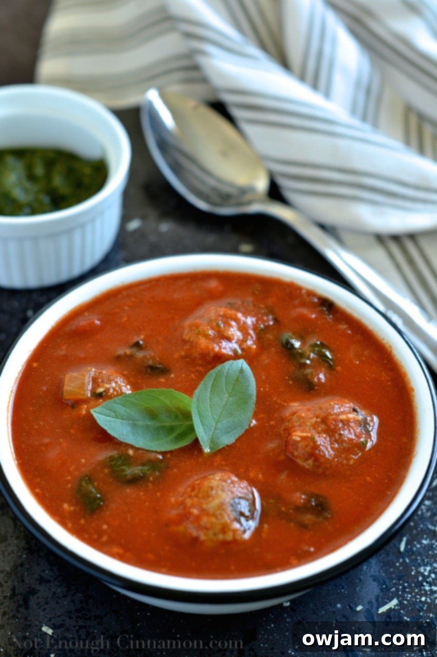 A bowl of creamy Spinach and Tomato Soup with Meatballs and a spoon, ready to be enjoyed.