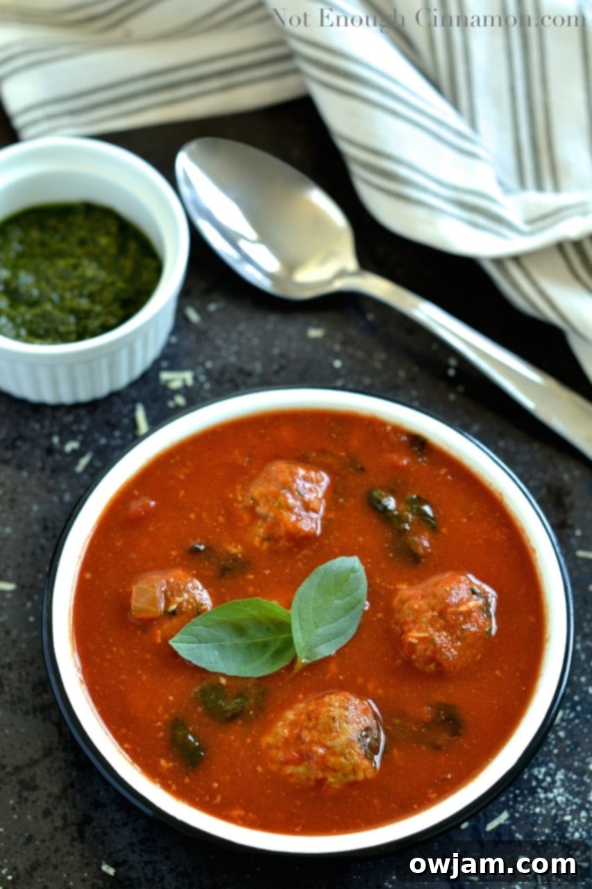 Spinach and Tomato Soup with Meatballs, garnished with a swirl of pesto and parmesan cheese.