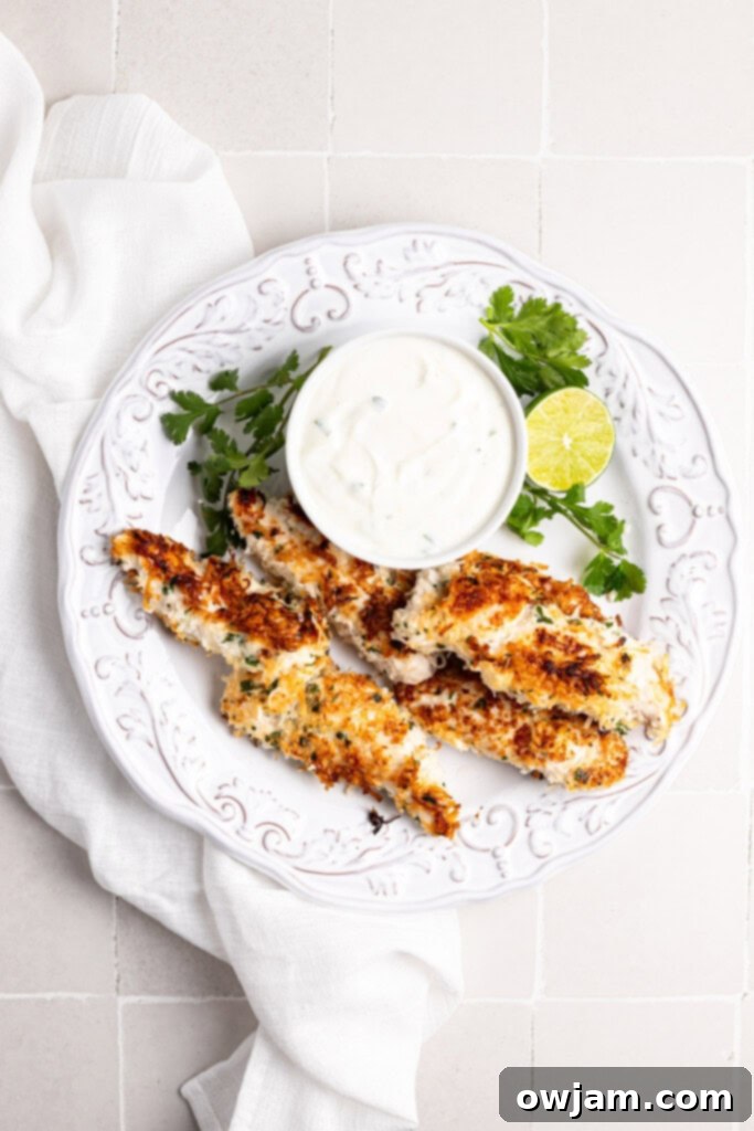 A serving of Coconut Chicken Tenders on a white plate with a side of creamy cilantro lime dipping sauce in a small bowl.