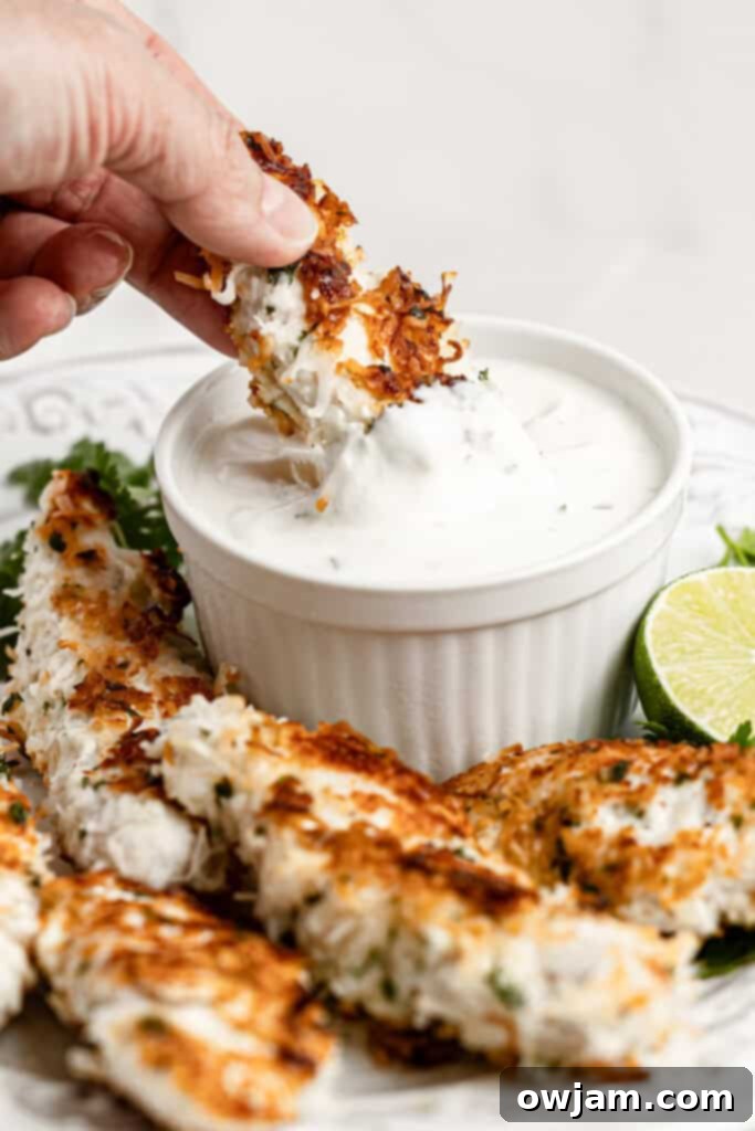 A close-up of a Coconut Chicken Tender being dipped into a creamy aioli sauce.