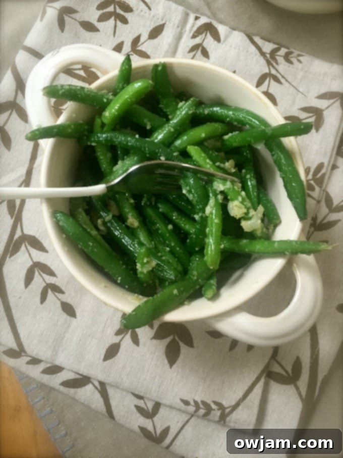 A close-up shot of hot garlic parmesan green beans, steam gently rising, in a white bowl.