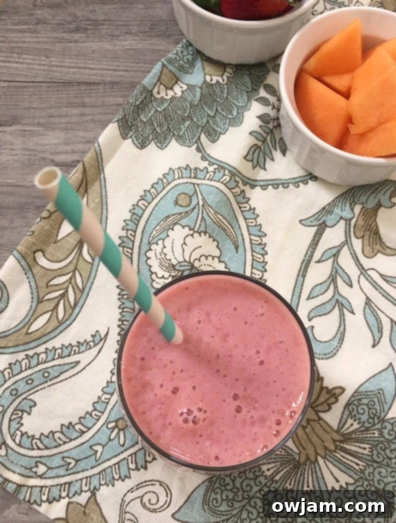 Strawberry Cantaloupe Smoothie in a clear glass with a straw, showing its inviting texture and color.