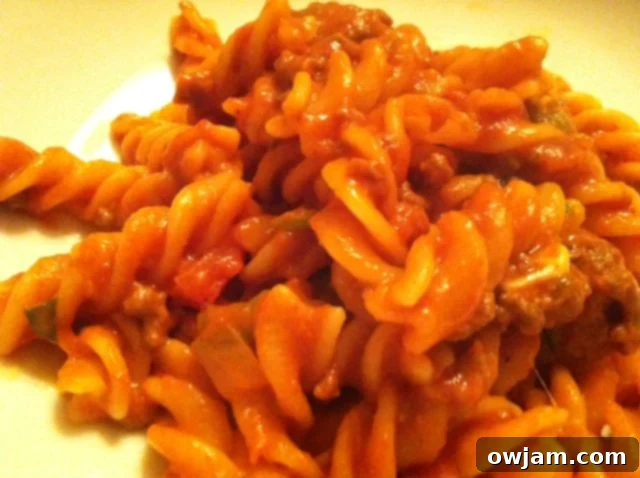 Cooked pasta being mixed thoroughly with the hearty goulash sauce, ensuring every piece is coated