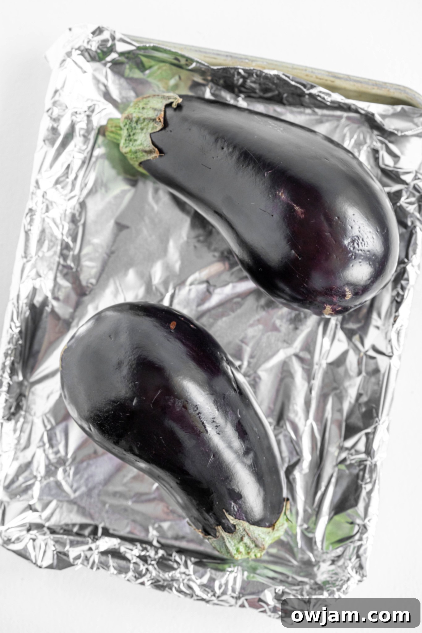 Whole eggplant with holes poked in the skin, ready for roasting on a baking tray.