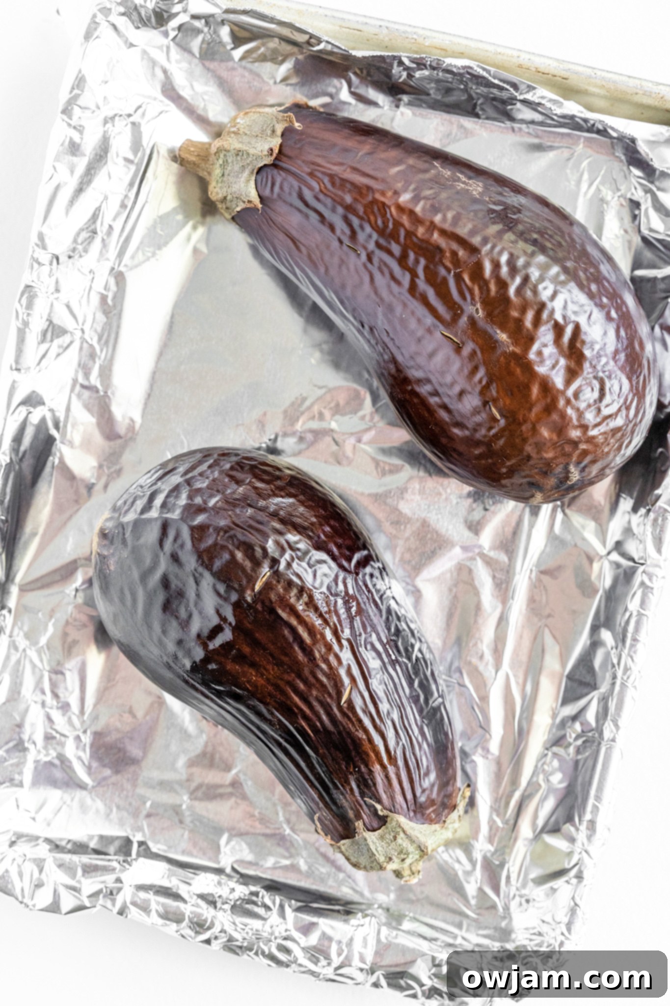 Roasted eggplant on a baking sheet, showing wrinkled skin after oven cooking.