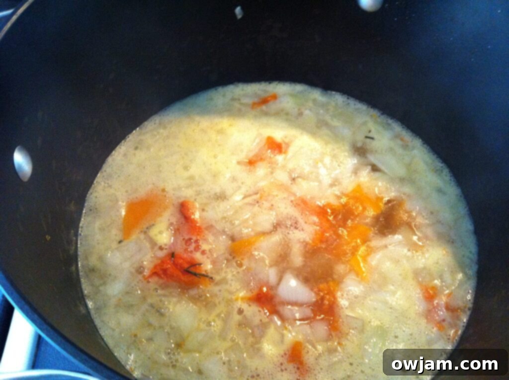 Butternut squash, chicken broth, sautéed onions, and garlic simmering in a pot, creating the base for the soup