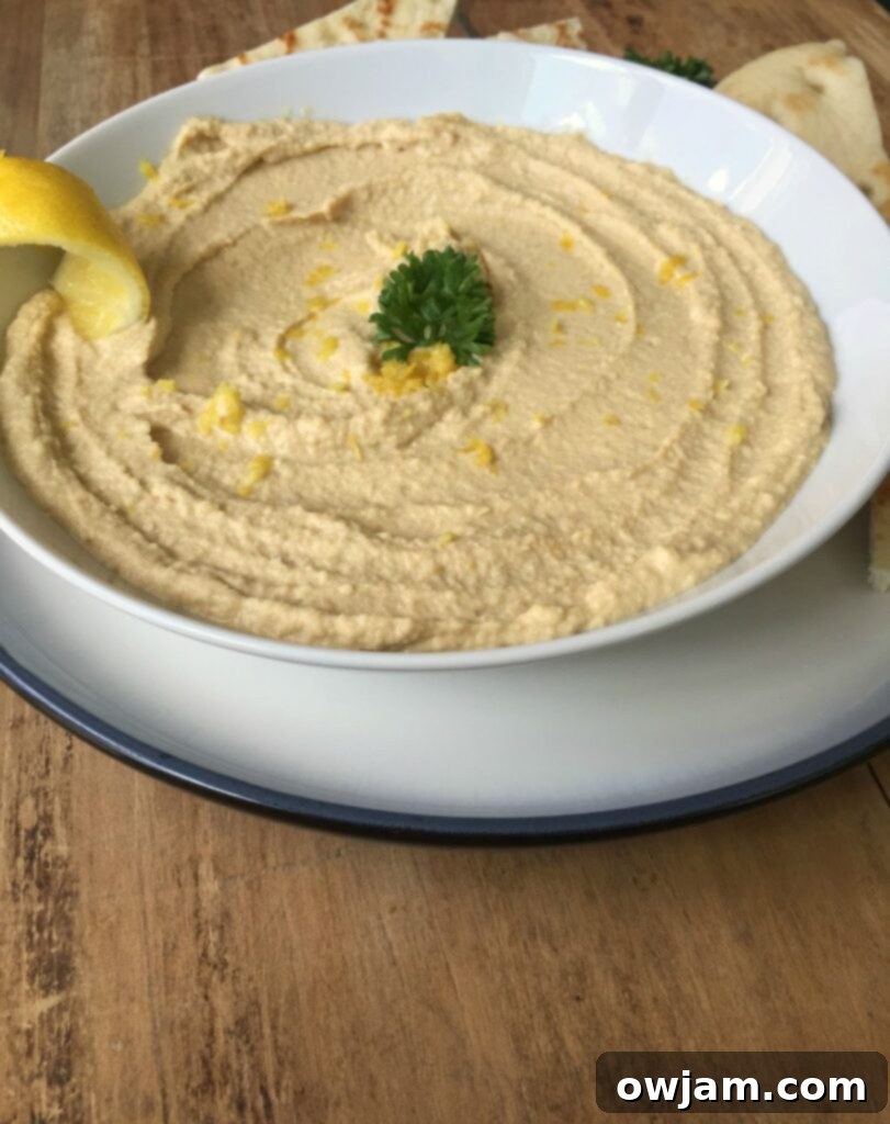 Zesty Lemon Hummus 3 A serving of creamy lemon hummus in a rustic bowl on a wooden board, garnished with lemon slices and parsley.