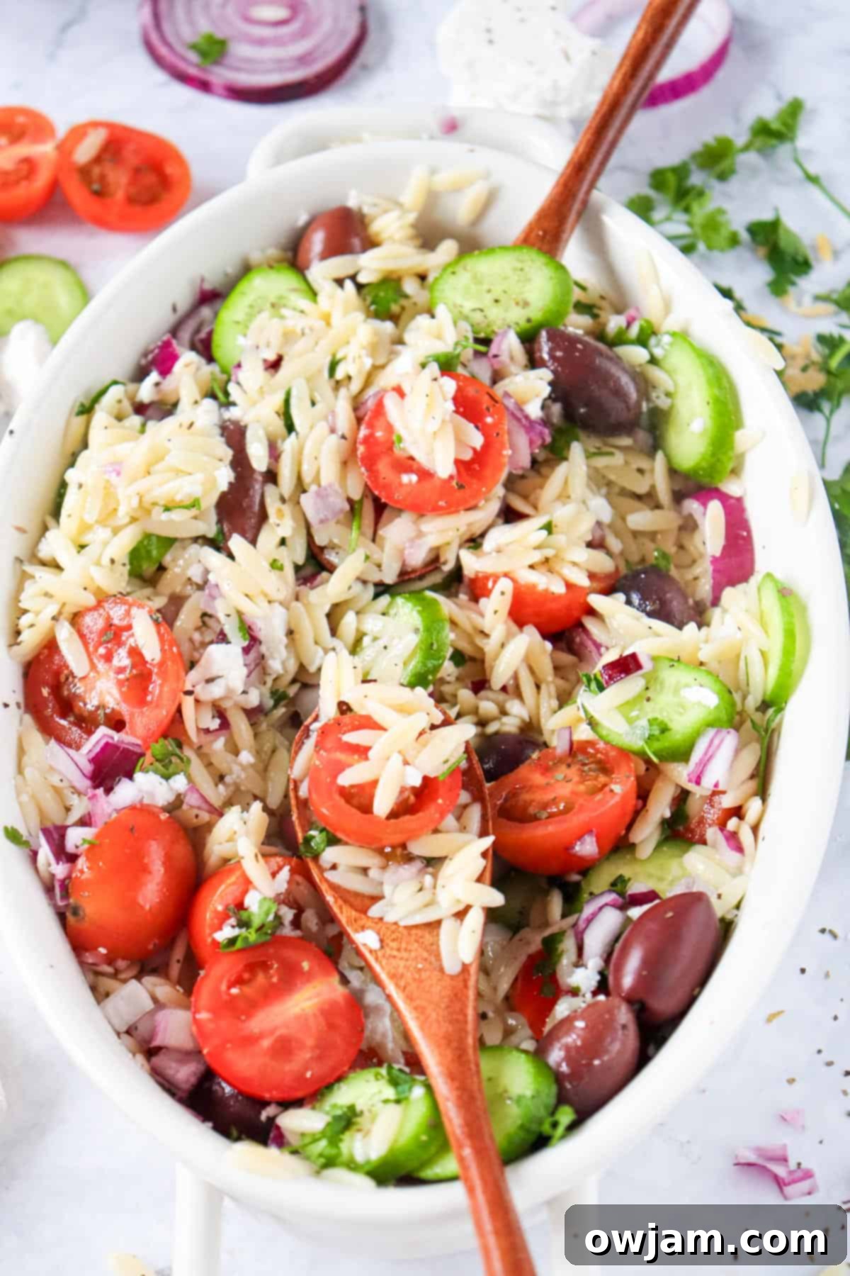 Zesty Mediterranean Orzo Salad 7 Greek Orzo Pasta Salad with a wooden spoon in a white serving bowl.
