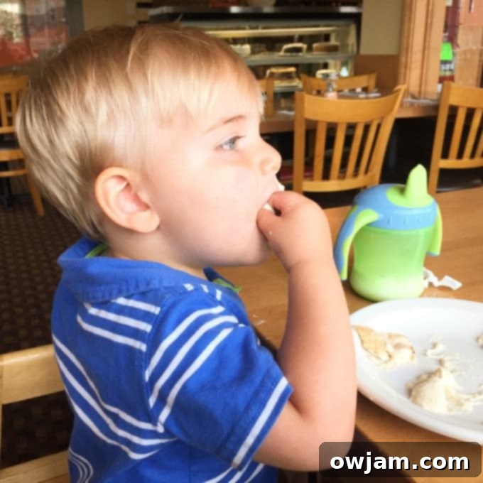 Happy child eating hummus directly from the container with his hands
