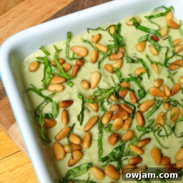 Basil Pesto Hummus with toasted pine nuts in a bowl, with fresh basil leaves