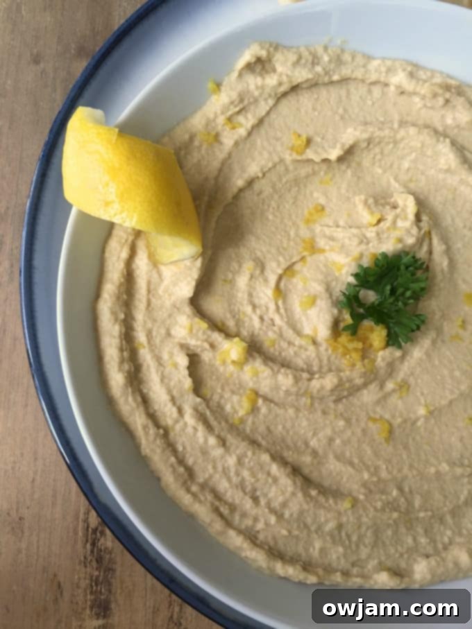 Bright Lemon Hummus in a white bowl, garnished with lemon zest and fresh herbs