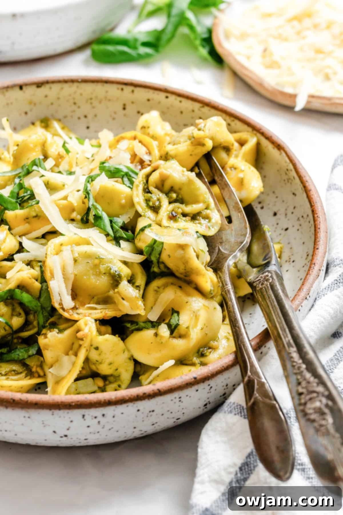 Speedy Cheesy Pesto Tortellini Dinner 2 tortellini in a bowl with a fork and knife resting on the side