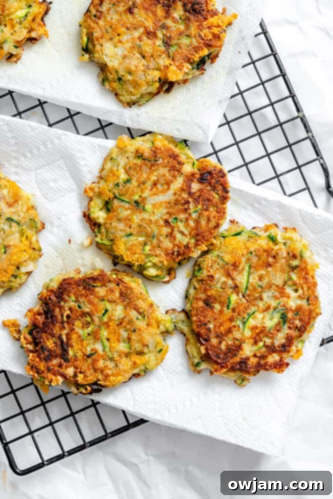 Effortless Zucchini Fritters 9 Cooked Easy Zucchini Fritters cooling on a wire rack with paper towels underneath, ready for serving.