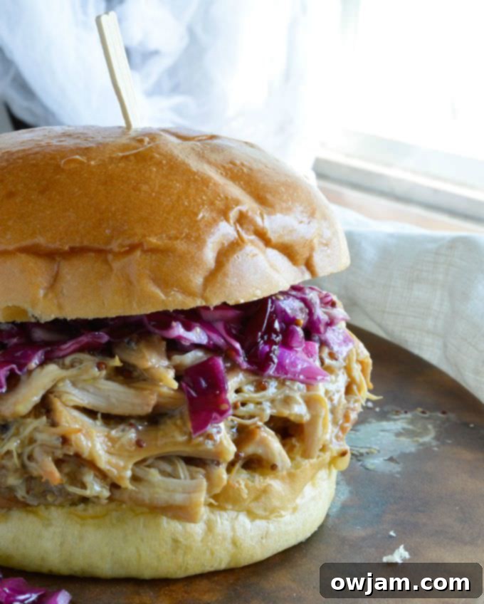 Close-up of a honey mustard shredded chicken sandwich, piled high on a bun with lettuce and tomato.