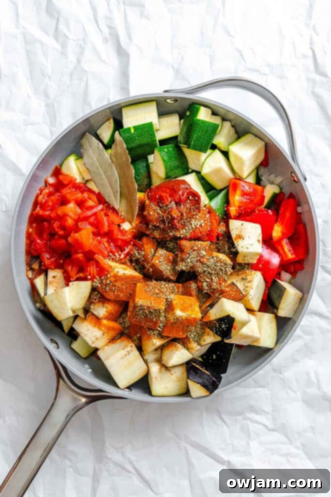Ratatouille vegetables and spices simmering in a large pan.