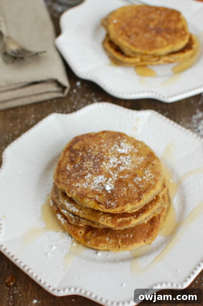 A close-up shot of a stack of golden-brown Pumpkin Pie Pancakes, showing their fluffy texture and enticing warm color, ready to be topped.