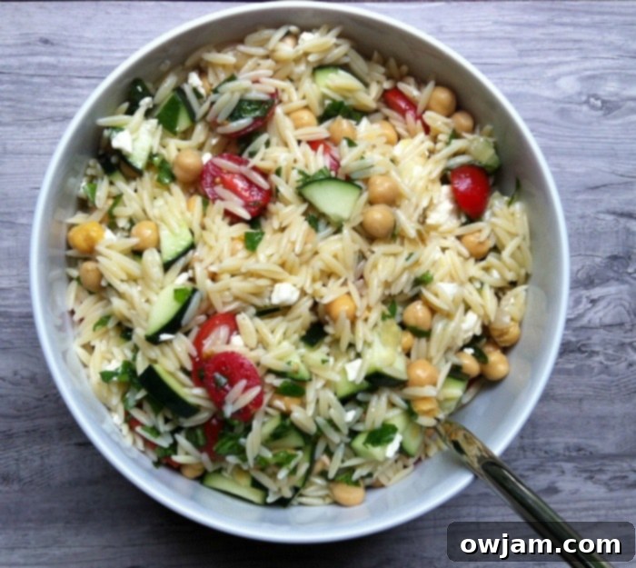 A refreshing and colorful summer orzo pasta salad, elegantly composed with juicy cherry tomatoes, crisp cucumber, crumbled feta cheese, and fragrant fresh herbs.