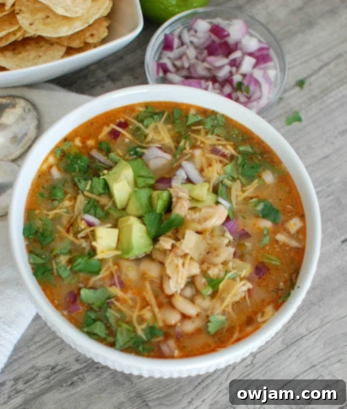Slow Cooker White Chicken Chili with a spoon and napkin, garnished with cheese.