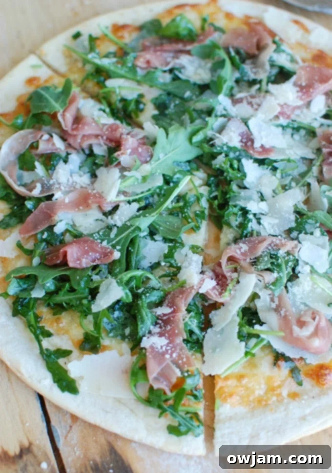 Peppery Arugula Prosciutto Pie 2 Prosciutto Arugula Pizza on a cutting board, garnished with fresh arugula and ready to be served.
