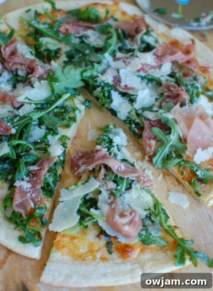 Peppery Arugula Prosciutto Pie 3 A slice of Prosciutto Arugula Pizza being lifted from the board, showcasing the fresh arugula and crispy crust.
