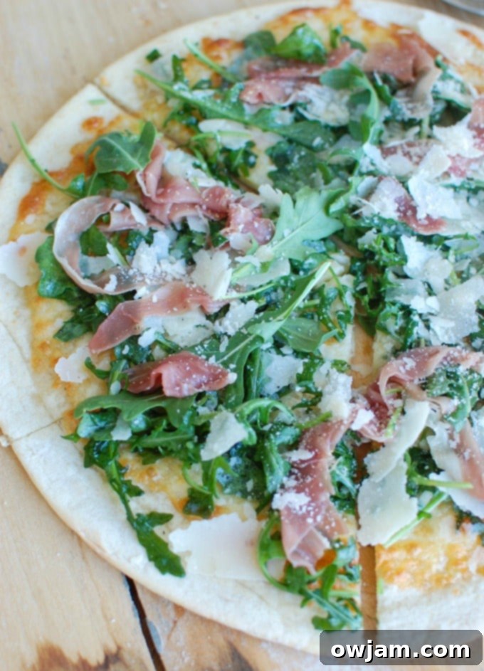 Peppery Arugula Prosciutto Pie 5 A freshly baked Prosciutto Arugula Pizza, generously garnished with fresh arugula and ready to be served.