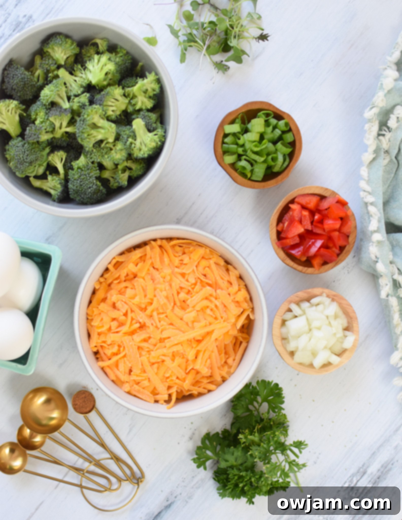 All the ingredients for Broccoli Cheddar Cups laid out on a table, including fresh broccoli, eggs, cheese, and vegetables.