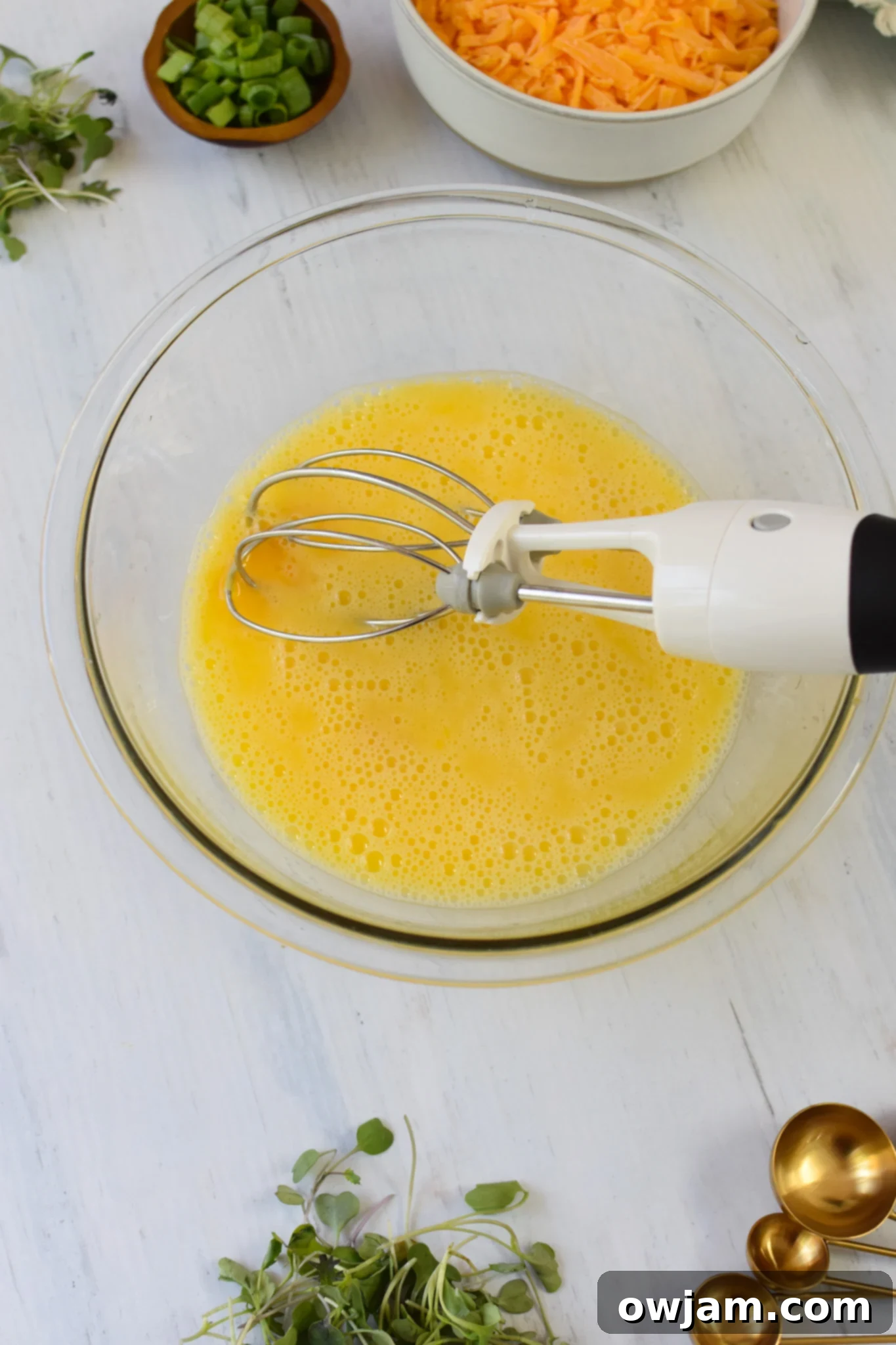 Eggs being whisked in a bowl with a hand whisk, showing the smooth, yellow consistency.