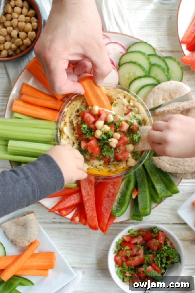 Delicious Lebanese Style Hummus topped with fresh tomatoes, parsley, mint, chickpeas, and pine nuts, served with pita bread and vegetables.