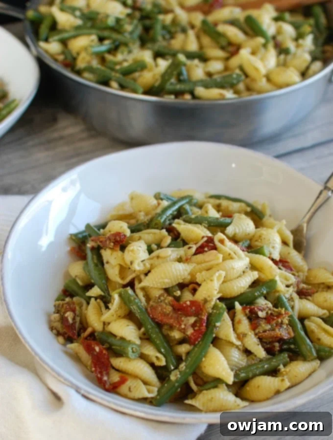 Pesto Pasta with Green Beans Sun-dried Tomatoes and Toasted Pine Nuts with spoon, showcasing the fresh, vibrant dish ready to be served.