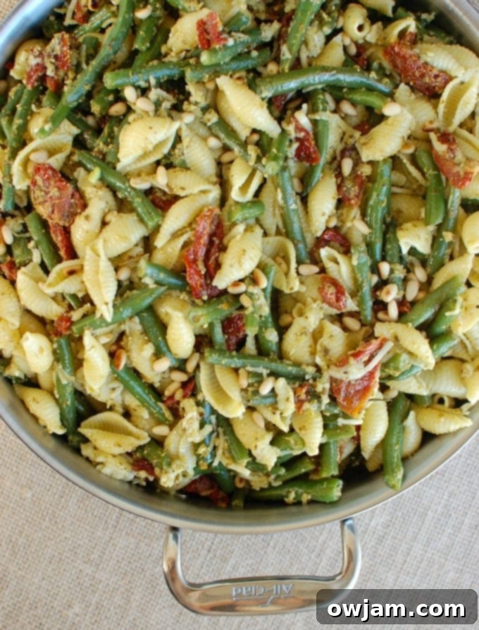 Pesto Pasta with Green Beans Sun-dried Tomatoes and Toasted Pine Nuts in pan, showing the vibrant ingredients mixed together.