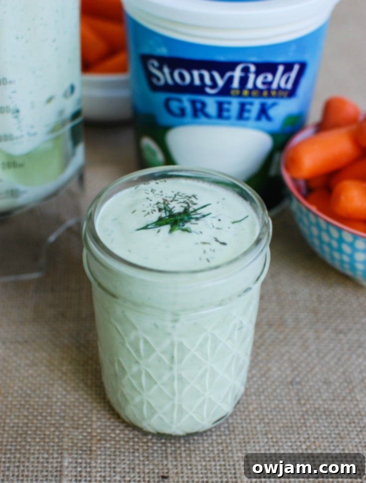 A close-up of Creamy Dill Sauce in a clear glass jar, showing the rich, thick texture and visible flecks of fresh green dill.