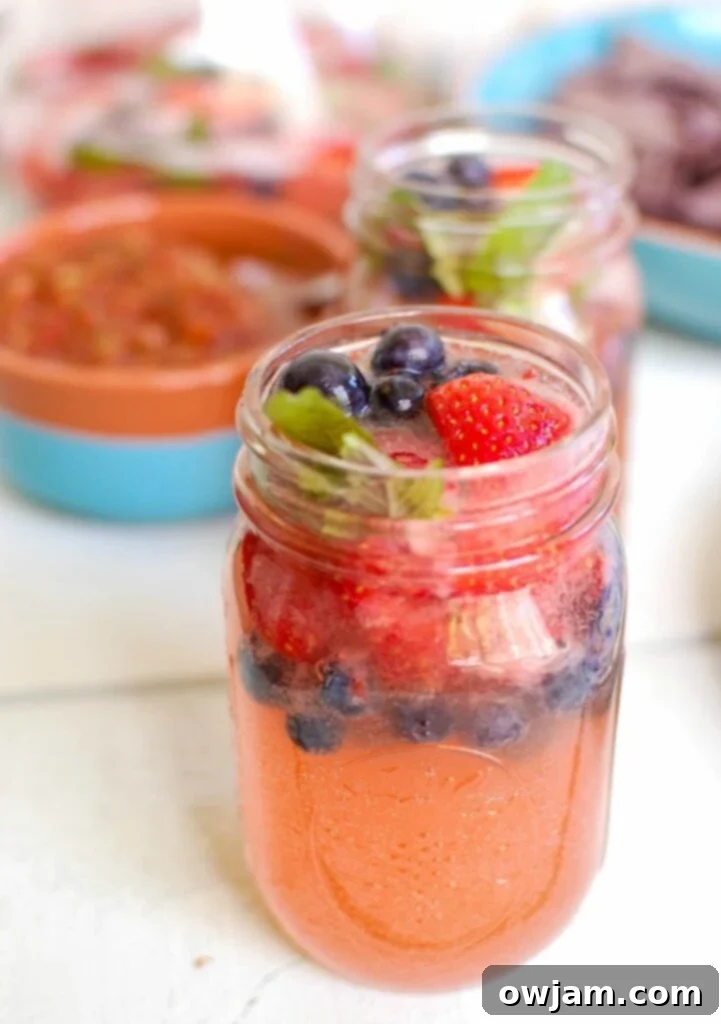 Strawberry Blueberry Lemonade Sparkler 2 Vibrant Strawberry Blueberry Lemonade Spritzer in a mason jar, garnished with fresh berries and mint, perfect for summer celebrations