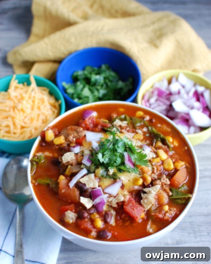 Set-It-and-Forget-It Turkey Kale Chili 2 A vibrant bowl of Slow Cooker Turkey Kale Chili garnished with sour cream, cilantro, and red onion, perfect for a cozy family meal or game day gathering.