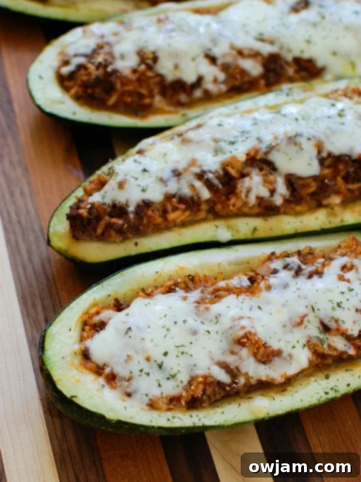 Vibrant Mediterranean Zucchini Boats 2 Mediterranean Zucchini Boats showcasing two halves of zucchini stuffed with meat and rice, topped with melted cheese and fresh parsley, on a white plate with a fork.