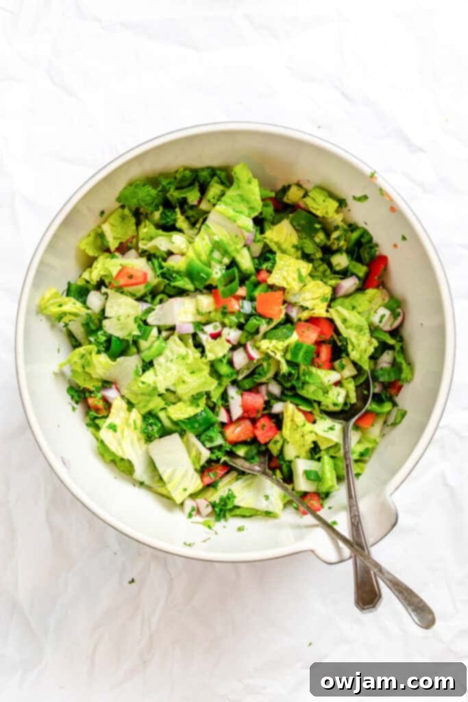 Tossing Fattoush Salad with tongs in a large bowl before dressing