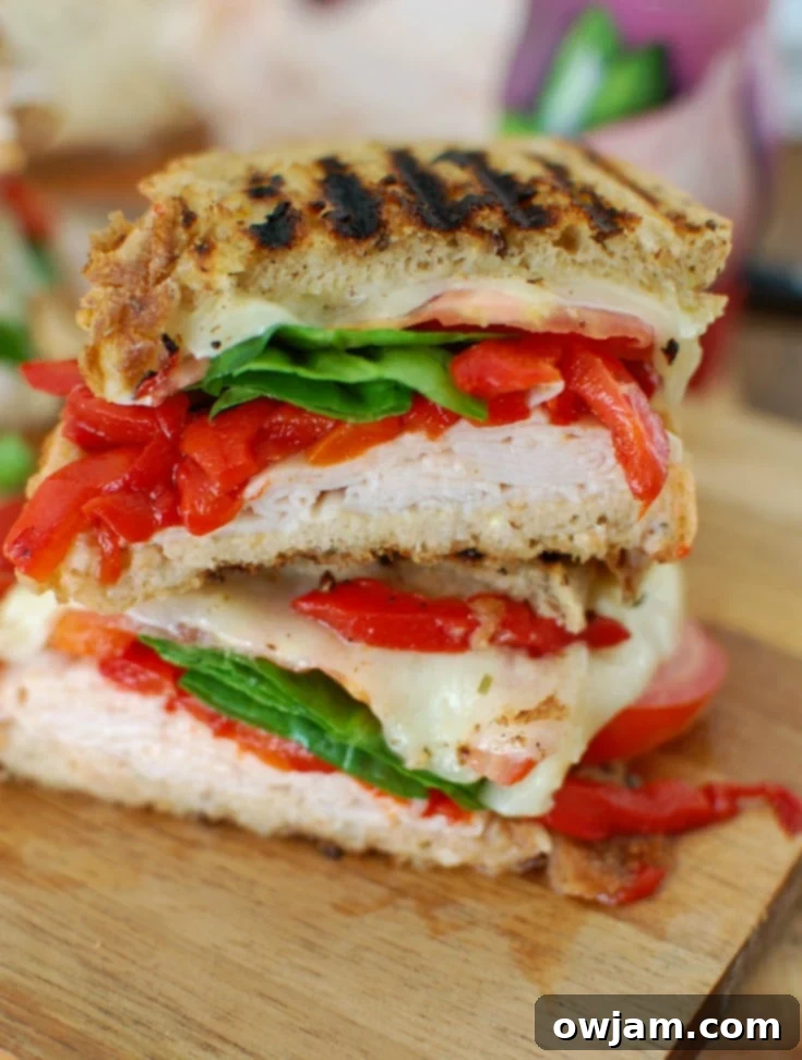 Mediterranean Turkey and Hummus Panini 3 Close-up of fresh ingredients for Mediterranean Turkey Hummus Panini: smoked turkey slices, roasted red peppers, spinach, sliced tomatoes, Havarti cheese, and artichoke hearts arranged on a cutting board.