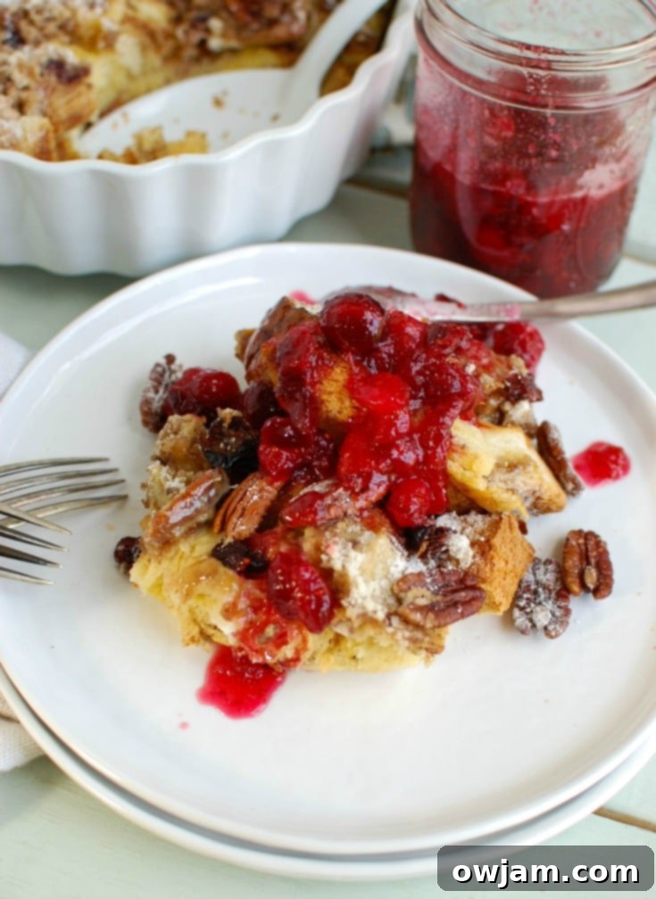 Golden-brown Overnight Eggnog French Toast Bake with a dusting of powdered sugar and a side of vibrant cranberry maple syrup, ready to be enjoyed on Christmas morning.