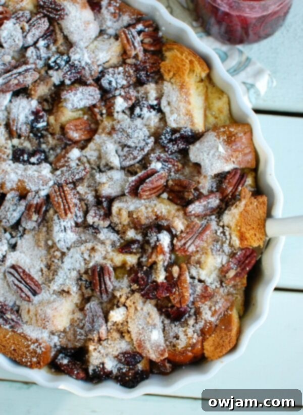 Individual serving of Overnight Eggnog French Toast Bake topped with powdered sugar and a generous drizzle of homemade cranberry maple syrup, ready to be devoured.