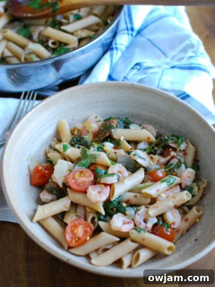 Zesty Shrimp Kale and Artichoke Pasta 2 A vibrant bowl of Shrimp Kale Artichoke Pasta, featuring pink shrimp, green kale, white artichoke hearts, and red cherry tomatoes tossed with pasta in a light lemon sauce, garnished with fresh parsley.