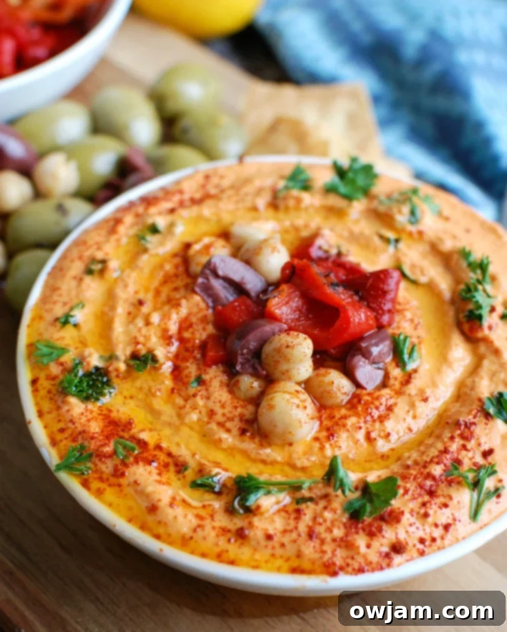 Creamy Roasted Red Pepper and Greek Yogurt Hummus 2 A vibrant bowl of Roasted Red Pepper Greek Yogurt Hummus, garnished with fresh parsley and a drizzle of olive oil, ready to be served with pita bread and sliced cucumbers.