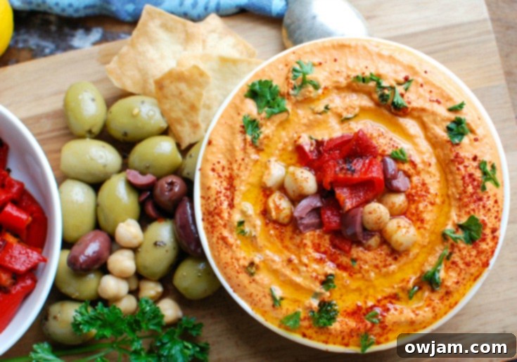 Creamy Roasted Red Pepper and Greek Yogurt Hummus 5 A bowl of Roasted Red Pepper Greek Yogurt Hummus, garnished with fresh herbs and olive oil, with pita bread on the side.