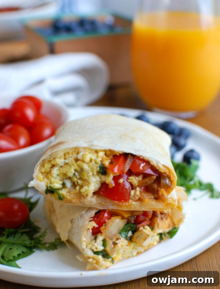 A delicious Vegetarian Breakfast Egg Burrito cut in half, revealing the egg and vegetable filling.