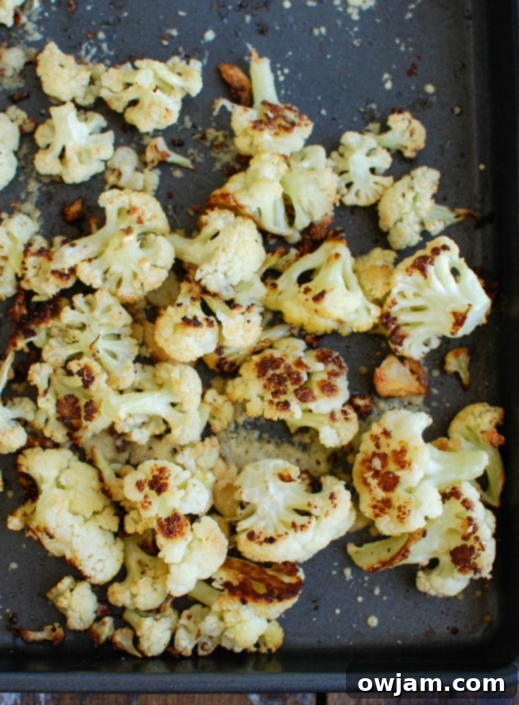 Crispy Parmesan Garlic Cauliflower 4 A serving of freshly roasted Parmesan Garlic Cauliflower, garnished with vibrant green parsley, showcasing its golden-brown edges and melted cheese. A delightful and healthy side.