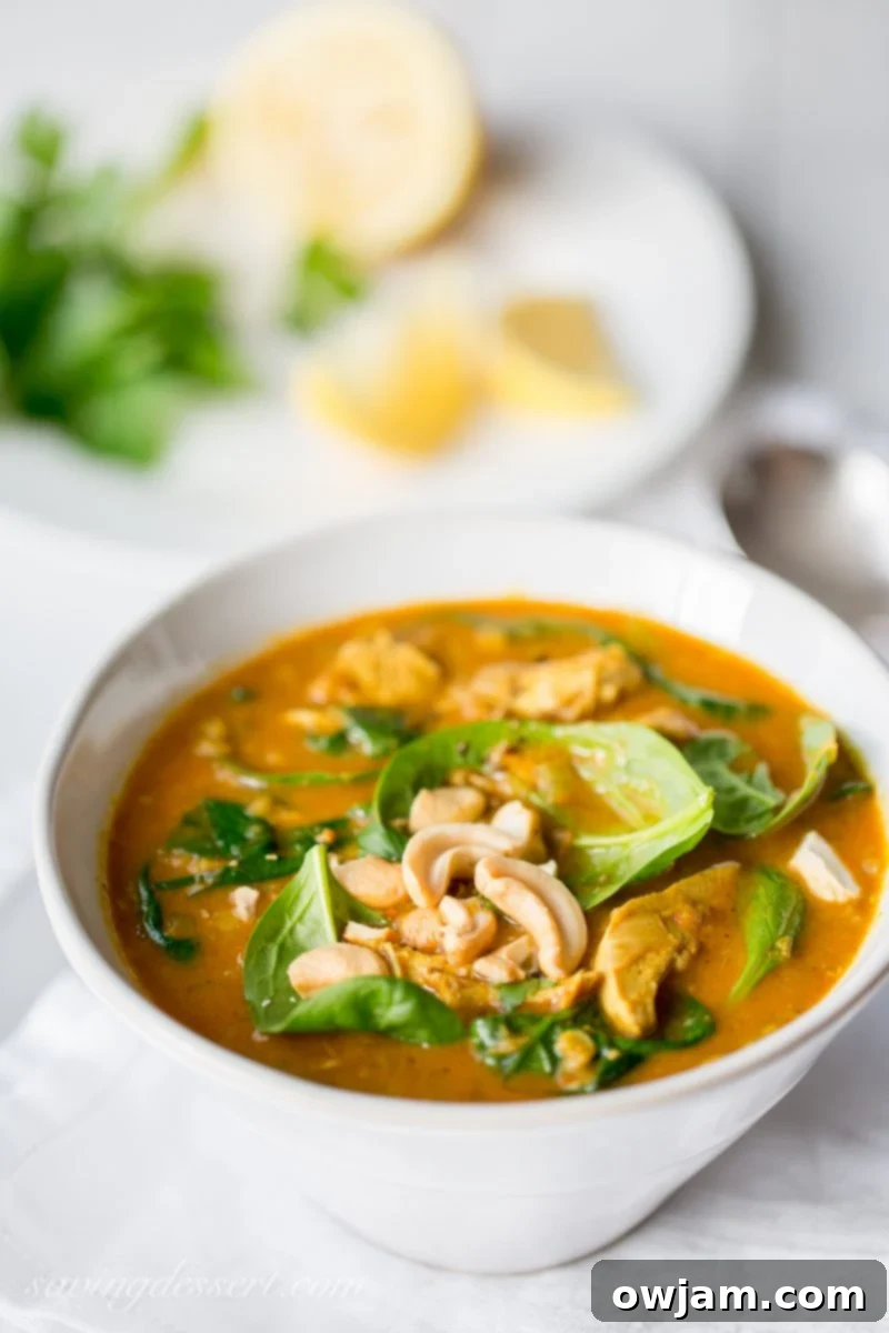 Creamy coconut chicken soup with spinach and lentils, served in a white bowl.