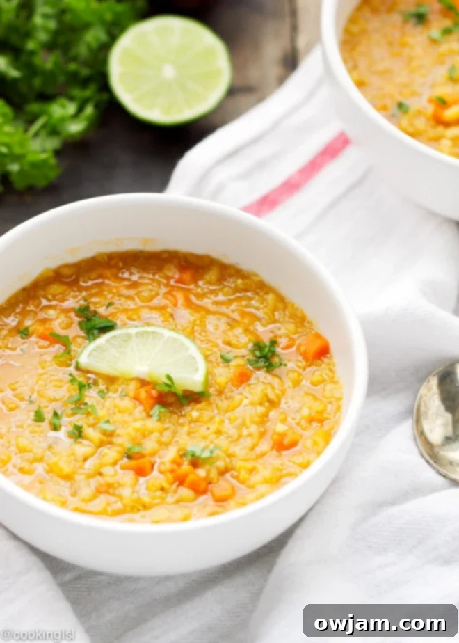 A bowl of curried red lentil and quinoa soup, garnished with fresh herbs.