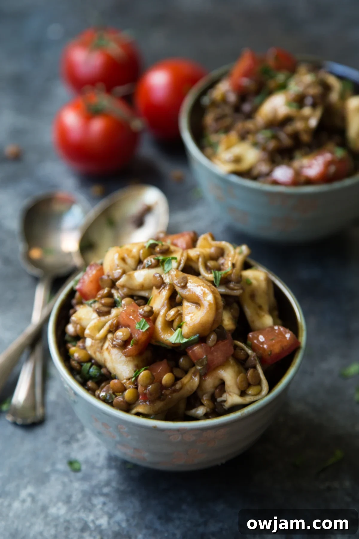 Lentil tortellini salad drizzled with balsamic vinaigrette, served in a white bowl.